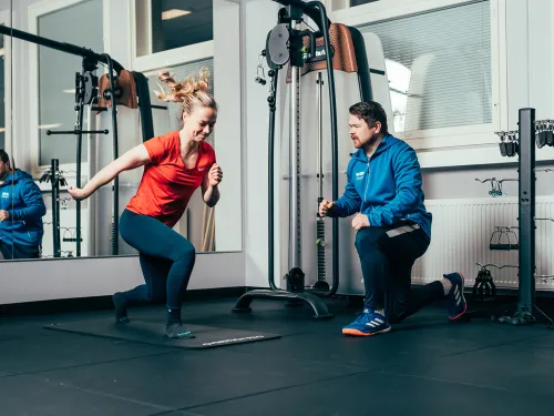 Woman exercising indoors while trainer observes.