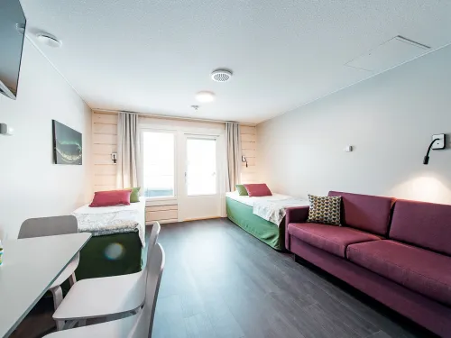 Valoisa hotelli­huone kahdella sängyllä, sohvalla ja parveke­näkymällä.