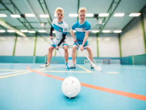 Kaksi salibandypelaajaa tavoittelee palloa sisätiloissa.