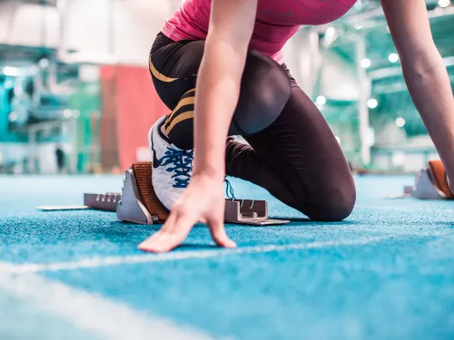 Athletes in starting position on blue indoor track.