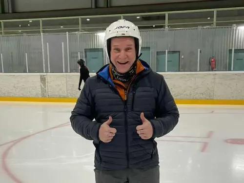 A man smiling and giving a thumbs-up on an ice rink, wearing a helmet and jacket.