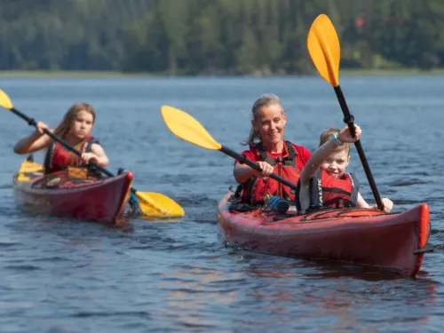 Kaksi kajakkia järvellä, aurinkoinen päivä, kaksi ihmistä kummassakin kajakissa.