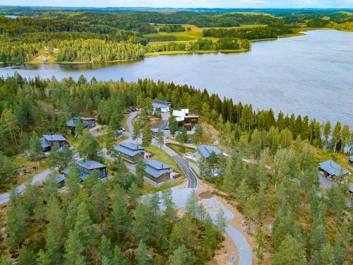 Ilmakuva metsän ympäröimästä järvimaisemasta ja mökeistä.