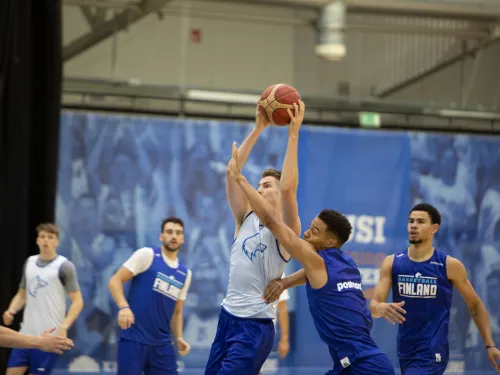 Koripallopelaajat kilpailevat pallosta sisähallissa.