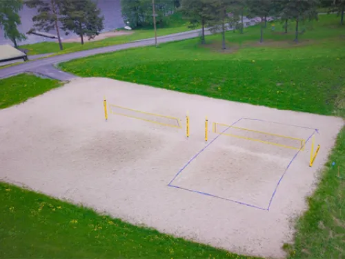 Hiekkapohjainen lentopallokenttä puistossa, vihreää nurmikkoa ympärillä.