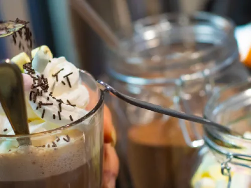 Kermavaahto koristeltu kuuma kaakao, käsi lusikoi koristeita.