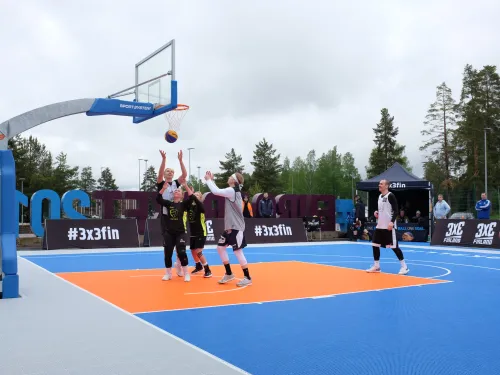 Ulkokoripallokentällä pelataan 3x3-ottelua. Pelaajat hyppäävät palloa tavoitellen.