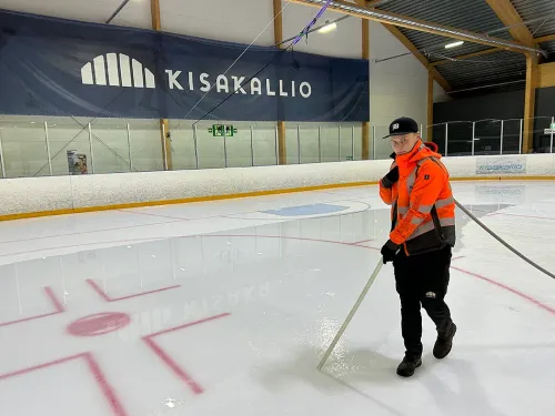 Henkilö huomiotakissa jääkiekkokaukalossa, taustalla Kisakallion logo.