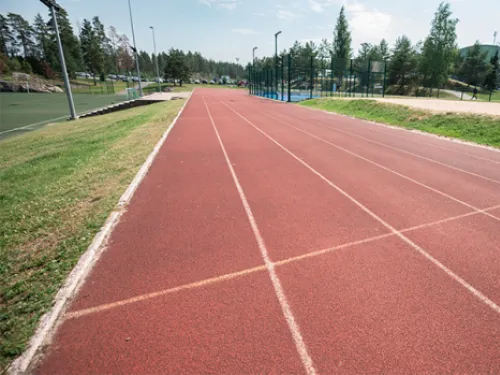 Punainen juoksurata, taustalla puita ja sininen taivas.