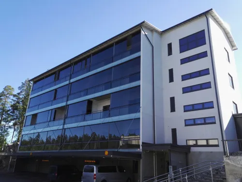 Kerrostalo, jossa on lasiseinä ja parkkitila alhaalla, kirkkaassa auringonpaisteessa.