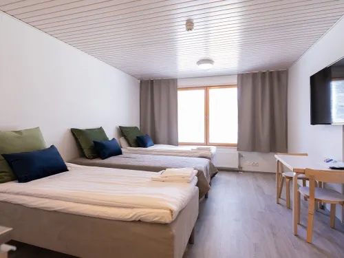 Kaksi vuodetta, pöytä, tuolit ja televisio vaaleassa huoneessa.