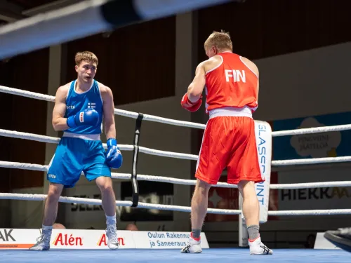 Kaksi nyrkkeilijää kehässä, toinen sininen, toinen punainen asu.