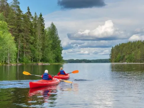 Kaksi henkilöä melomassa punaisilla kajakeilla järvellä metsän ympäröimänä.