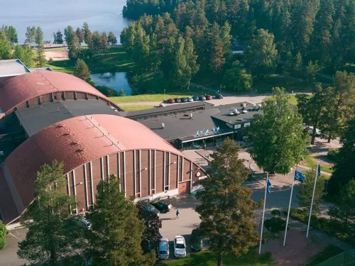 Punakattoinen rakennus vehreässä ympäristössä, taustalla järvimaisema.