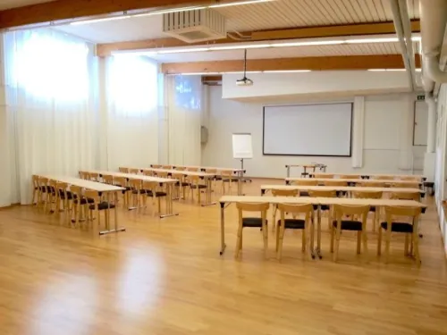 Tyhjä luokkahuone puulattialla, pöydät ja tuolit siistissä järjestyksessä.