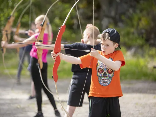 Lapsia jousiampumassa ulkona, keskittyneet ilmeet.