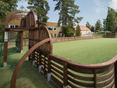 Suljettu nurmikenttä, puukaiteet, taustalla puita ja rakennuksia.