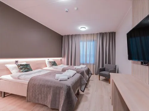 Kaksi sänkyä hotellihuoneessa, iso televisio seinällä.