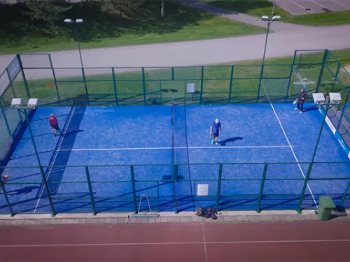 Sininen padel-kenttä, neljä pelaajaa, kirkas päivä.