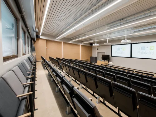 Tyhjä nykyaikainen luentosali, jossa on rivissä tuoleja ja kaksi näyttöä edessä.