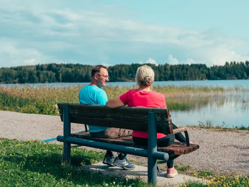 Pariskunta istuu penkillä järven rannalla.