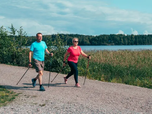 Pariskunta sauvakävelee järven rannalla.