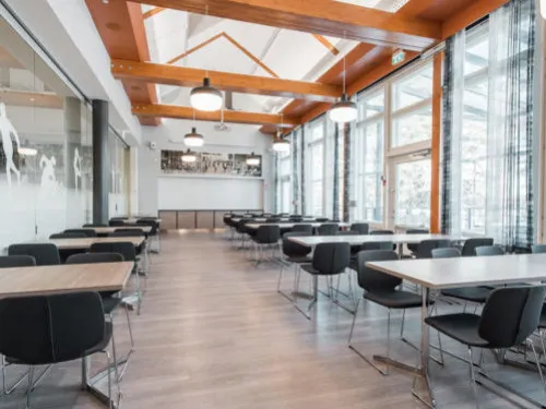 Avara kahvila, vaaleat puupalkit, mustat tuolit, isot ikkunat.