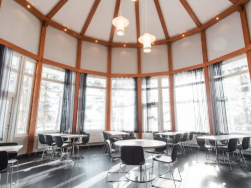 Pyöreä huone suurella ikkunaseinällä ja valaisimilla, tyhjiä pöytiä ja tuoleja.