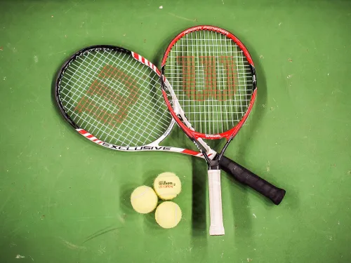 Tennismailat kentällä maassa ristikkäin ja kolme tennispalloa vieressä