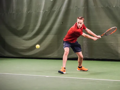 Tennispelaaja lyömässä palloa sisäkentällä.