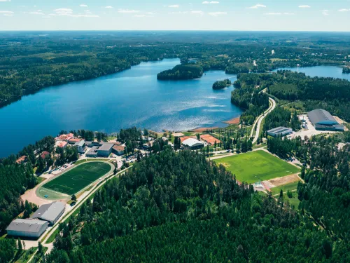 Ilmakuva järvestä ja metsäisestä maisemasta, jossa urheilukenttiä ja rakennuksia.