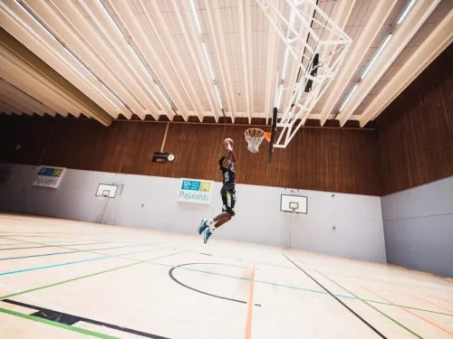 Koripalloilija hyppäämässä kohti koria tyhjässä sisähallissa.