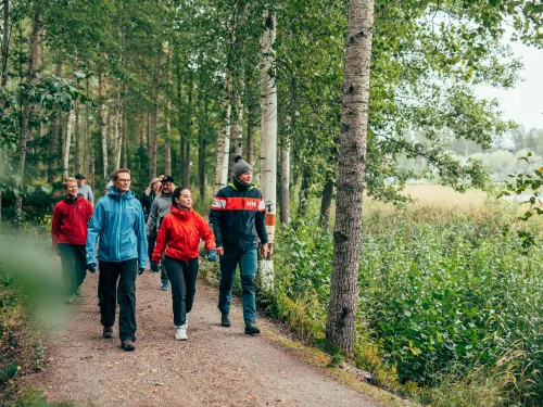 Ryhmä ihmisiä kävelee metsäpolulla kesäpäivänä.