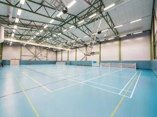 Tyhjä liikuntahalli, vaaleansiniset lattiat, koripallokorit, kattovalot.