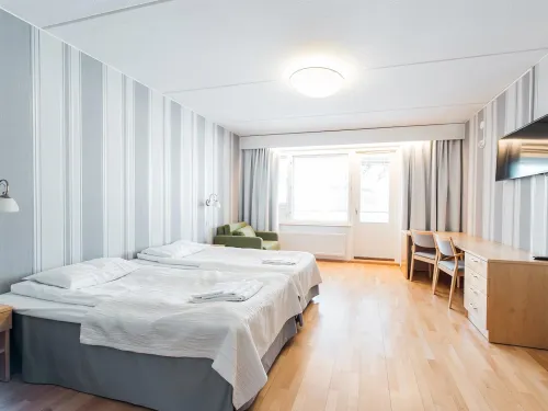 Kaksi sänkyä, vaalea huone, ikkuna, kirjoituspöytä ja tuoli.