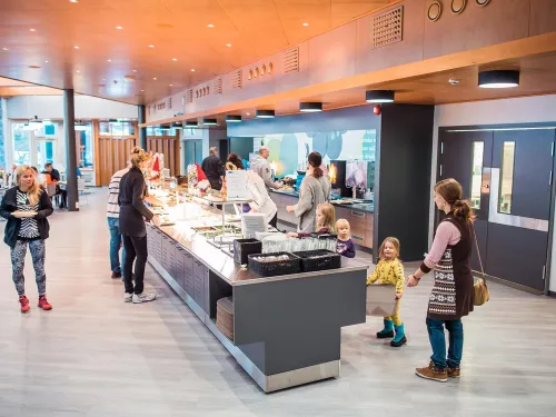 Valoisassa ravintolassa ihmisiä buffetin äärellä, lapset ja aikuiset ruokailemassa.