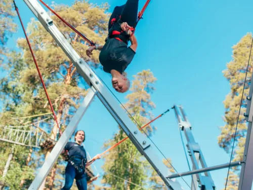 Henkilö benji-trampoliinilla metsätaustalla.