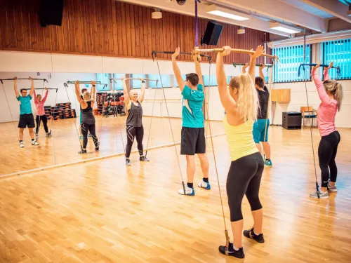 Treeniryhmä seisoo peilisalissa nostaen painotankoja ilmaan.