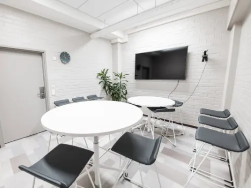 Tyylikäs kokoushuone, kaksi pyöreää pöytää, tuoleja ja seinällä televisio.