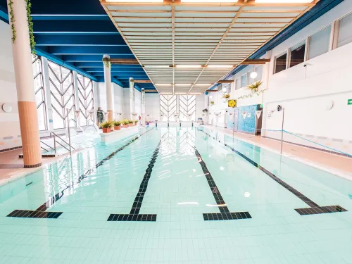 Sisäuima-allas, vaaleansininen vesi, valaistus, ja raidat pohjassa.