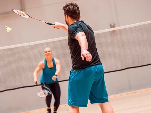 Kaksi henkilöä pelaamassa sulkapalloa sisähallissa.