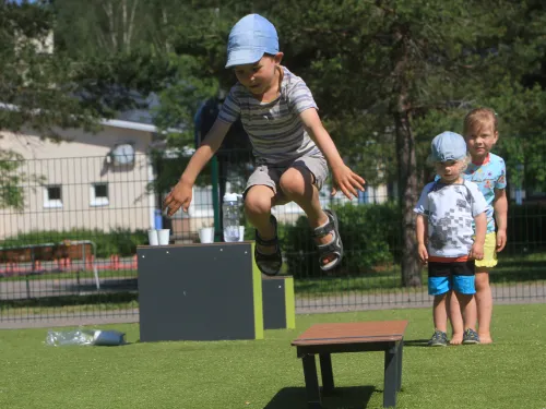 Child jumping off a small platform, two kids watch in the background.