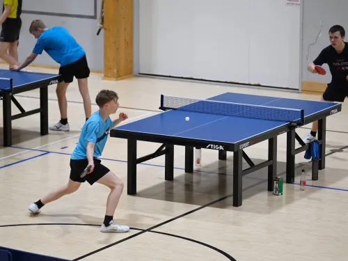 Kaksi henkilöä pelaa pöytätennistä sisätiloissa.