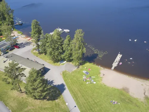 Ilmakuva rannasta, jossa ihmisiä nurmikolla ja laituri järvelle.