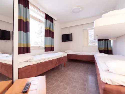 Hostellihuone, jossa kaksi sänkyä ja kerrossänky, kirkas valaistus.