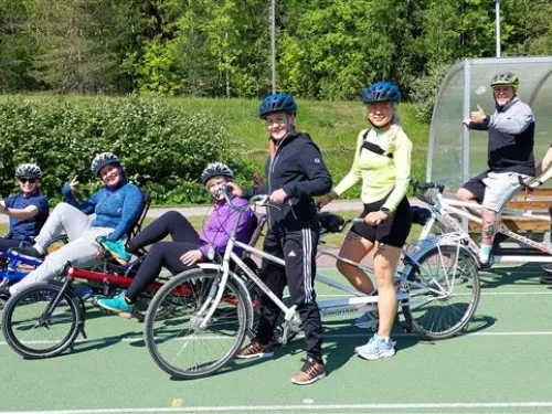 Joukko ihmisiä pyöräilemässä ulkokentällä, kaikki kypärissä.