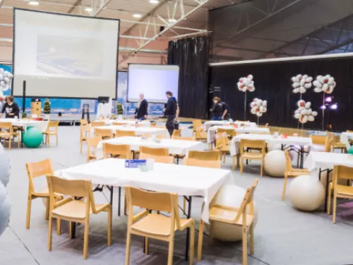 Messuhalli, jossa on pöytiä, tuoleja ja suuria ilmapalloja.