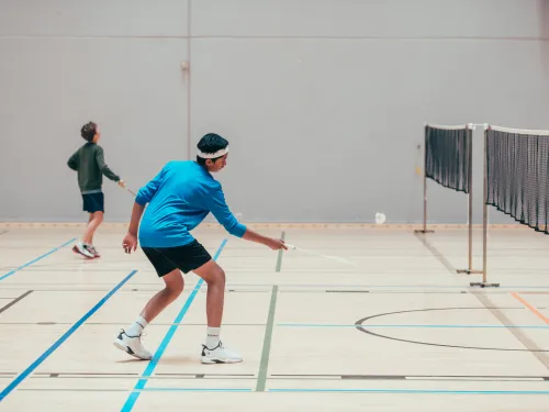 Kaksi miestä pelaamassa sulkapalloa sisätiloissa.