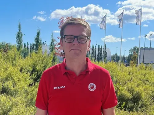 Mies punaisessa paidassa, taustalla vihreää kasvillisuutta ja sininen taivas.
