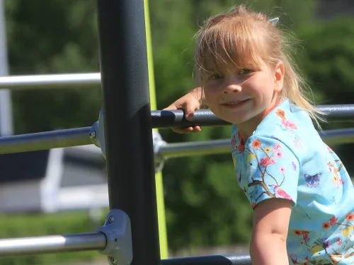 Child smiling while climbing playground bars outdoors.